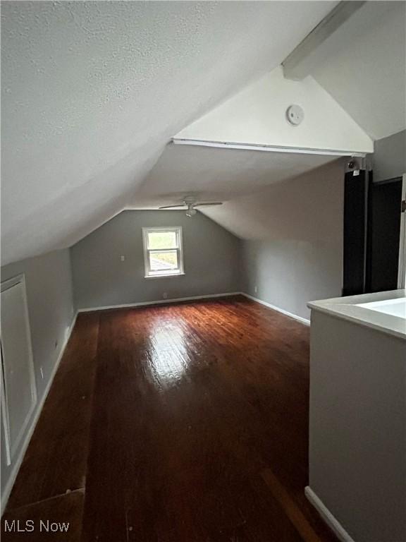 bonus room with dark wood-style floors, vaulted ceiling with beams, a textured ceiling, and baseboards