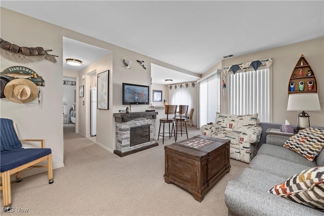 living area featuring visible vents, baseboards, lofted ceiling, carpet floors, and a stone fireplace