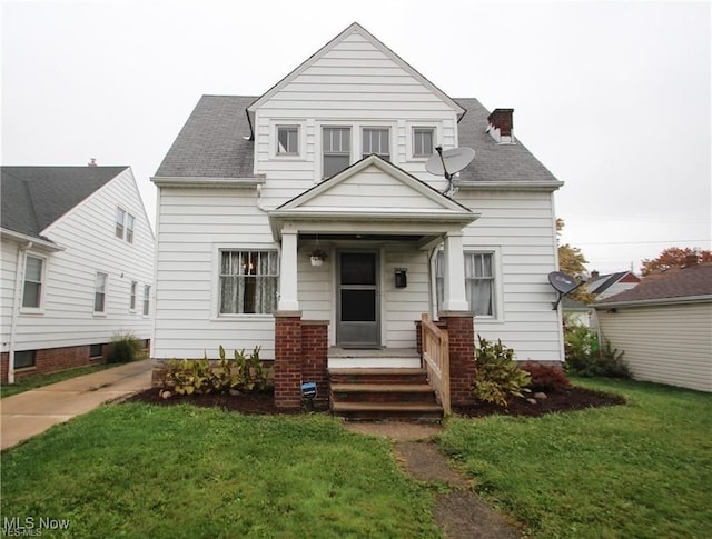 view of front of house with a porch, a front yard, roof with shingles, and a chimney