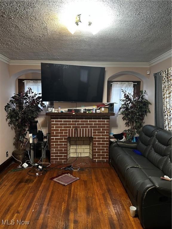 living area with a brick fireplace, wood-type flooring, a textured ceiling, and crown molding