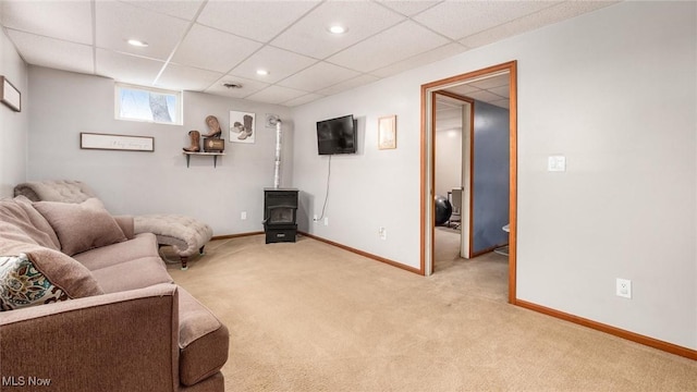 living area featuring a paneled ceiling, recessed lighting, light colored carpet, baseboards, and a wood stove