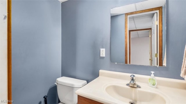 half bath with a drop ceiling, vanity, and toilet