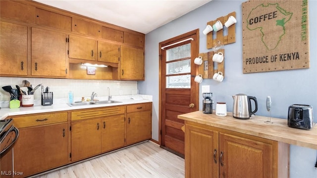 kitchen with stove, a sink, light countertops, backsplash, and brown cabinetry