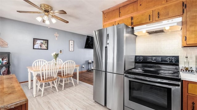 kitchen featuring under cabinet range hood, stainless steel appliances, light countertops, brown cabinets, and tasteful backsplash