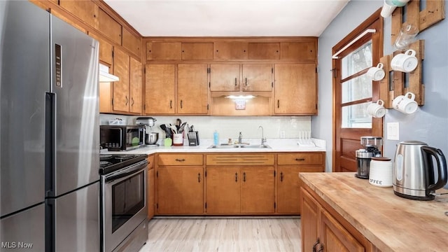 kitchen featuring stainless steel appliances, light countertops, light wood-style floors, brown cabinetry, and a sink