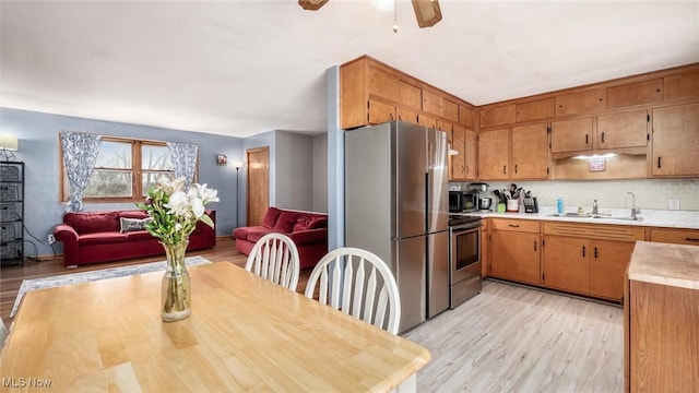 kitchen with brown cabinetry, appliances with stainless steel finishes, open floor plan, light countertops, and a sink