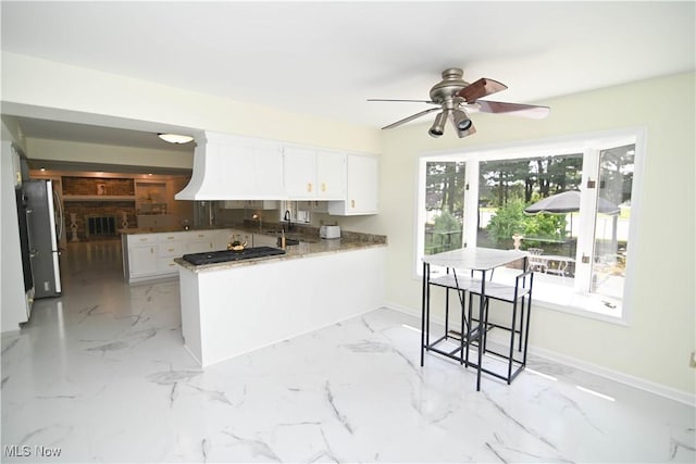 kitchen featuring white cabinets, freestanding refrigerator, a peninsula, marble finish floor, and a sink