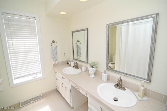 bathroom featuring tile patterned flooring, visible vents, a sink, and double vanity