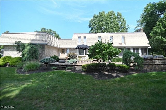 back of house featuring a yard, mansard roof, and brick siding