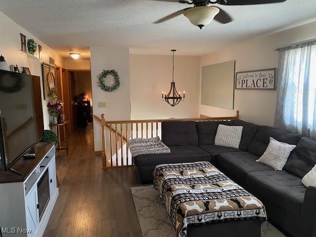 living room featuring ceiling fan with notable chandelier, a textured ceiling, and wood finished floors