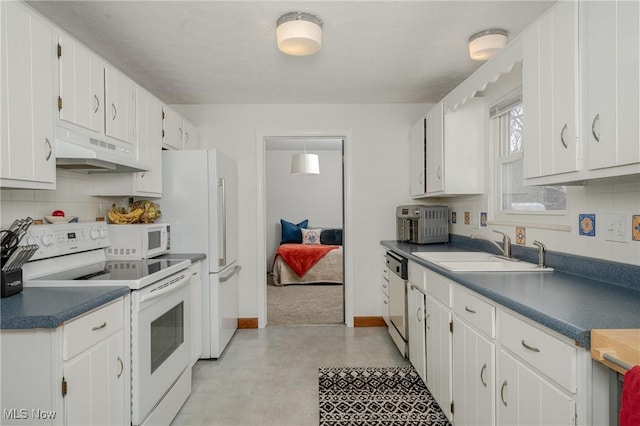 kitchen with white appliances, dark countertops, under cabinet range hood, white cabinetry, and a sink