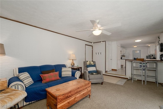 living area featuring a textured ceiling, carpet floors, ornamental molding, and a ceiling fan