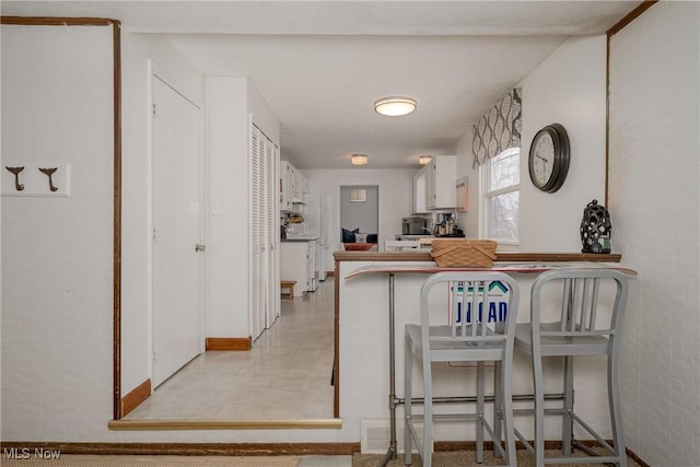 kitchen featuring a peninsula, a kitchen bar, and white cabinets