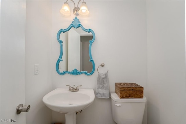 half bath with a sink, toilet, and a notable chandelier