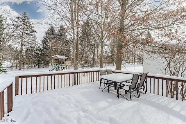 snow covered deck featuring outdoor dining area and a playground