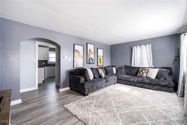 living area featuring arched walkways, wood finished floors, and baseboards