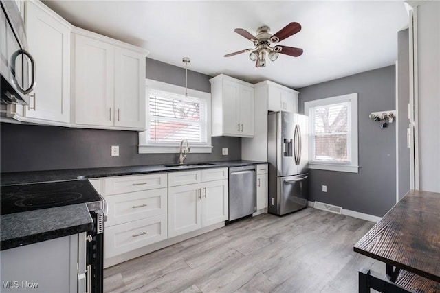 kitchen with stainless steel appliances, a sink, white cabinetry, dark countertops, and pendant lighting