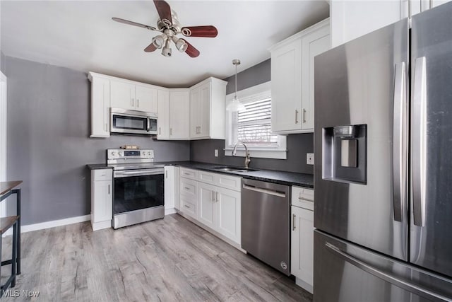 kitchen with stainless steel appliances, dark countertops, a sink, and white cabinetry