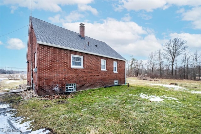 view of side of home with roof with shingles, brick siding, a lawn, and a chimney