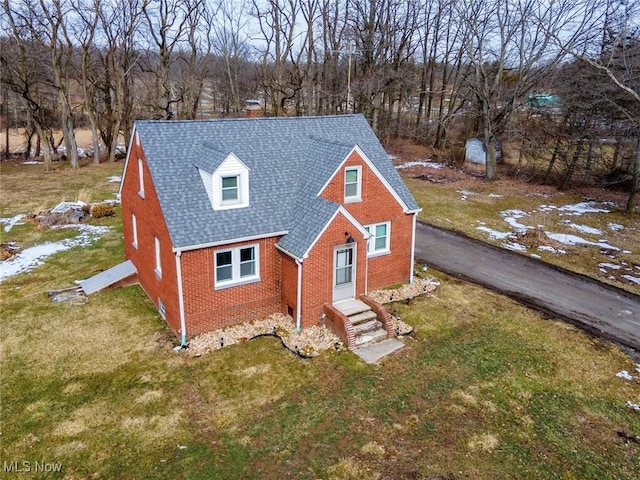 view of front of property featuring brick siding, roof with shingles, and a front yard