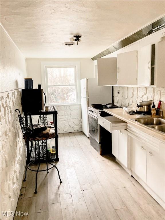 kitchen with a sink, freestanding refrigerator, gas range oven, white cabinets, and light wood-style floors