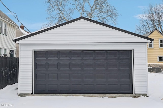 snow covered garage featuring a garage and fence