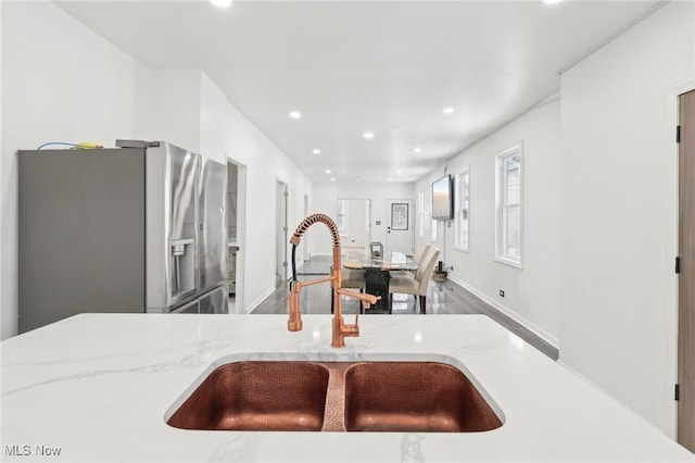 kitchen featuring recessed lighting, light stone countertops, a sink, wood finished floors, and stainless steel fridge