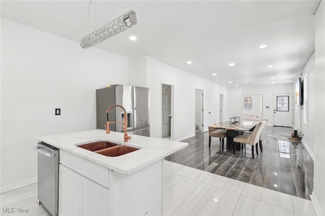 kitchen featuring white cabinets, an island with sink, appliances with stainless steel finishes, light countertops, and a sink