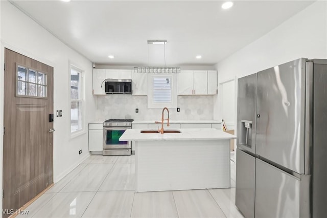 kitchen with decorative light fixtures, a center island with sink, appliances with stainless steel finishes, white cabinetry, and a sink