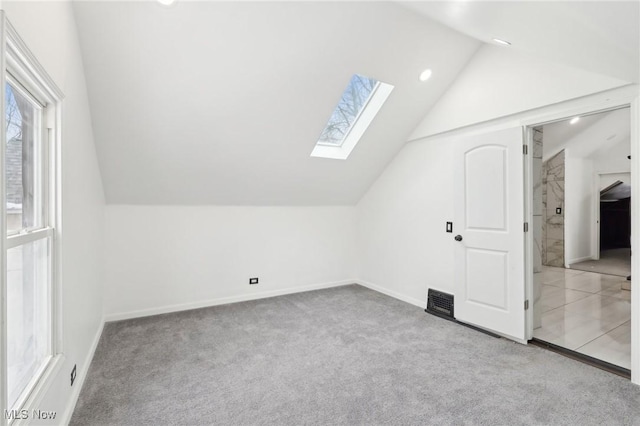 additional living space featuring vaulted ceiling with skylight, light carpet, and baseboards