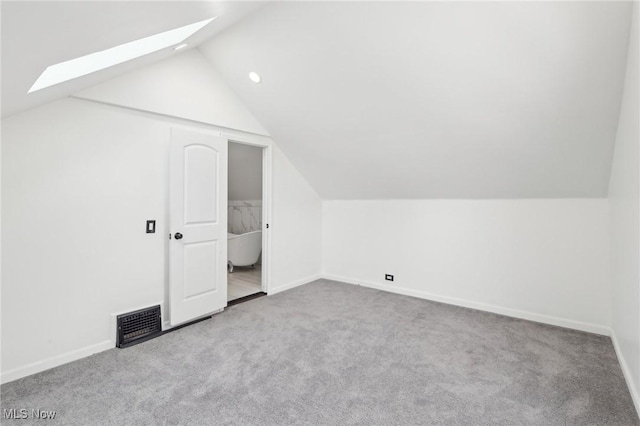 additional living space featuring light carpet, vaulted ceiling with skylight, visible vents, and baseboards