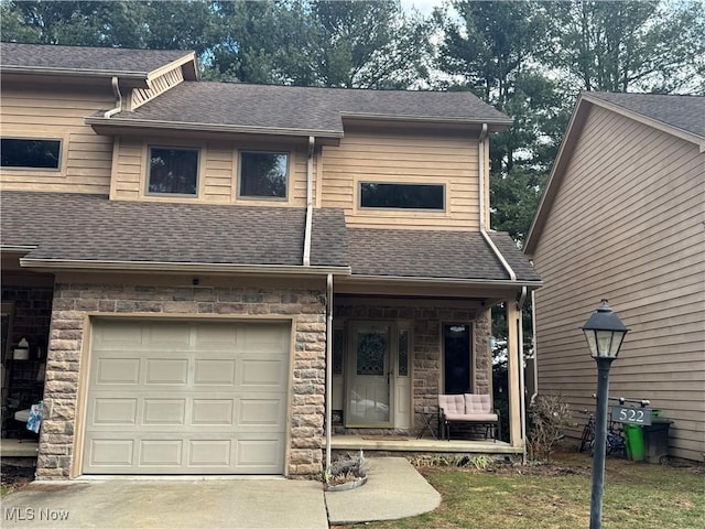 view of front of property featuring stone siding, roof with shingles, driveway, and an attached garage