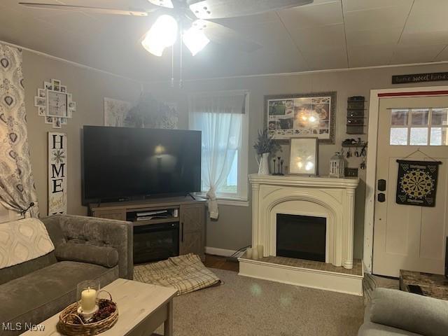 living area featuring a fireplace with raised hearth and a ceiling fan