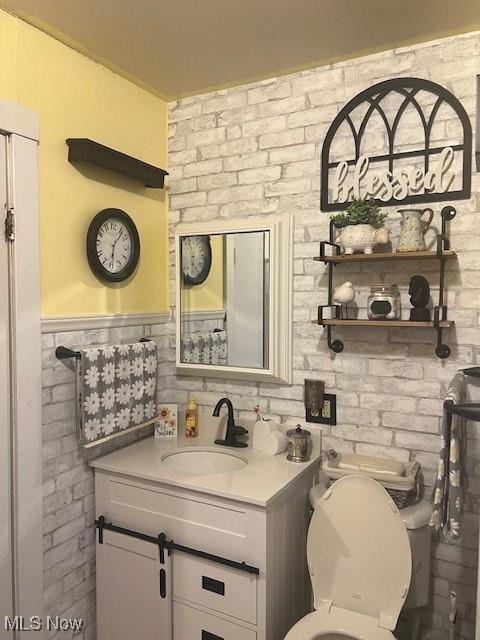 half bathroom featuring brick wall, vanity, and toilet