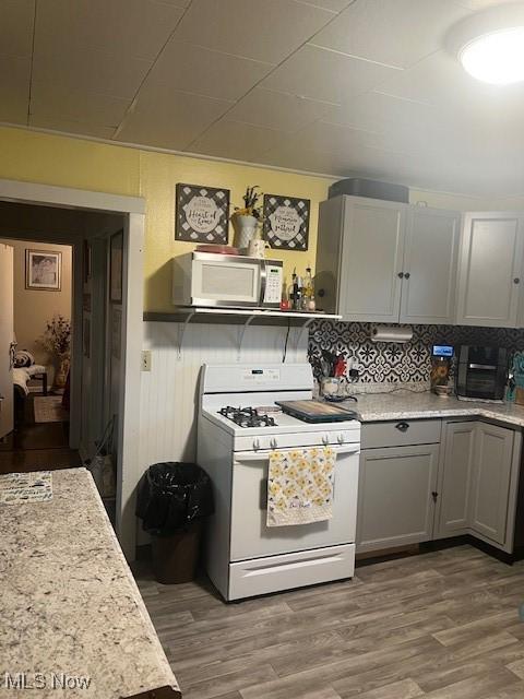 kitchen featuring white appliances, backsplash, light countertops, and wood finished floors