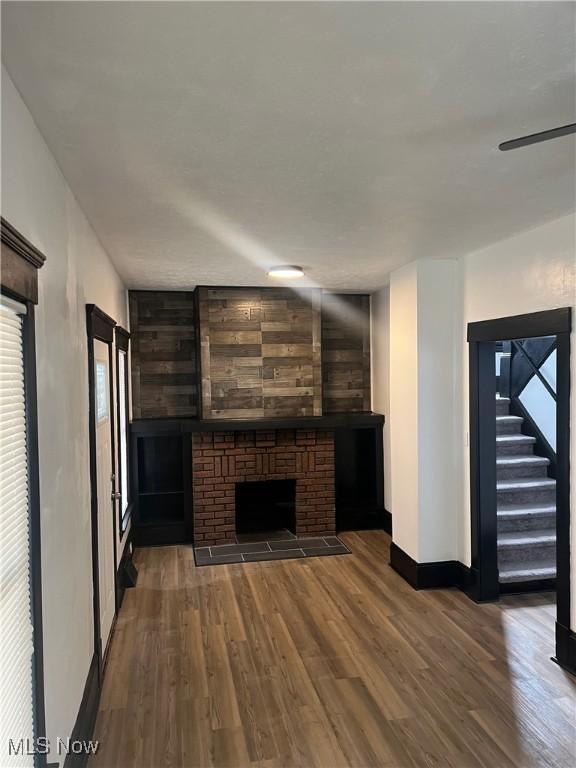 unfurnished living room featuring ceiling fan, dark wood-type flooring, baseboards, stairway, and a brick fireplace