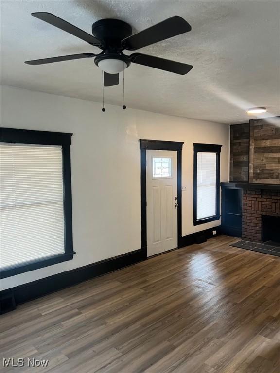 unfurnished living room featuring a brick fireplace, a textured ceiling, baseboards, and wood finished floors