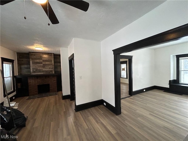 unfurnished living room with a brick fireplace, a textured ceiling, baseboards, and wood finished floors