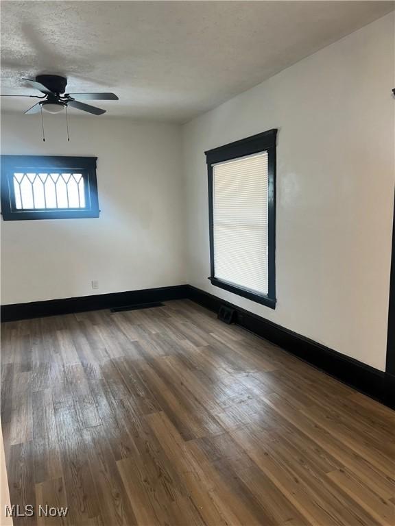 empty room with a ceiling fan, a textured ceiling, baseboards, and wood finished floors