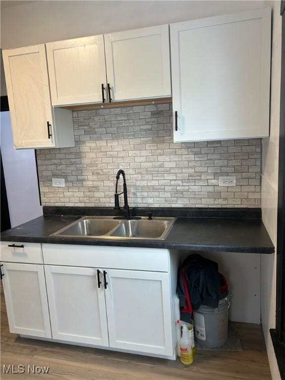 kitchen featuring dark countertops, light wood-style flooring, backsplash, white cabinetry, and a sink