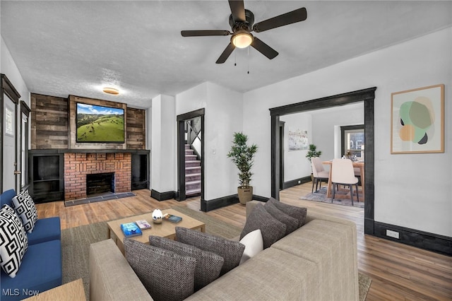 living area with a fireplace, a textured ceiling, baseboards, and wood finished floors