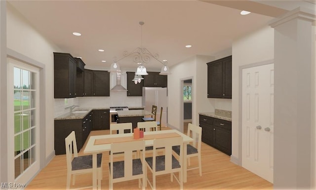 kitchen featuring pendant lighting, light wood-style flooring, freestanding refrigerator, a sink, and wall chimney exhaust hood