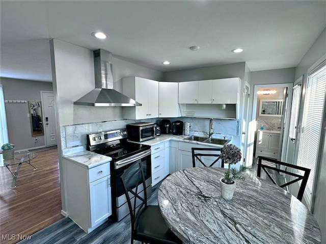 kitchen with white cabinets, stainless steel appliances, light countertops, wall chimney range hood, and a sink