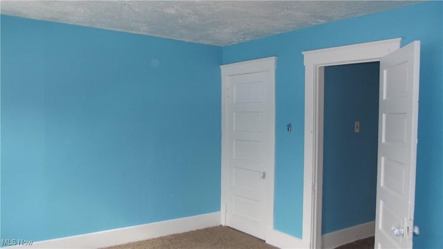 carpeted empty room with a textured ceiling and baseboards