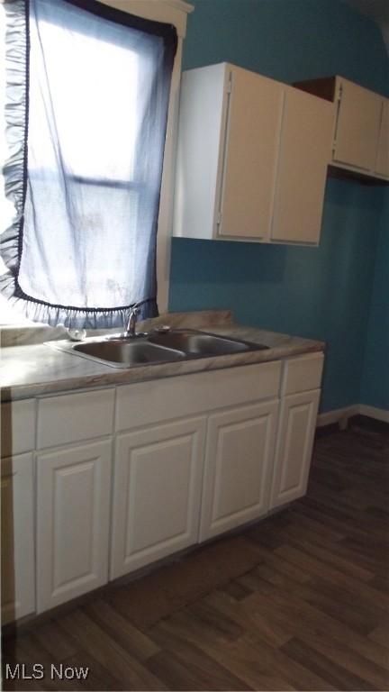 kitchen with baseboards, dark wood-style flooring, white cabinets, and a sink