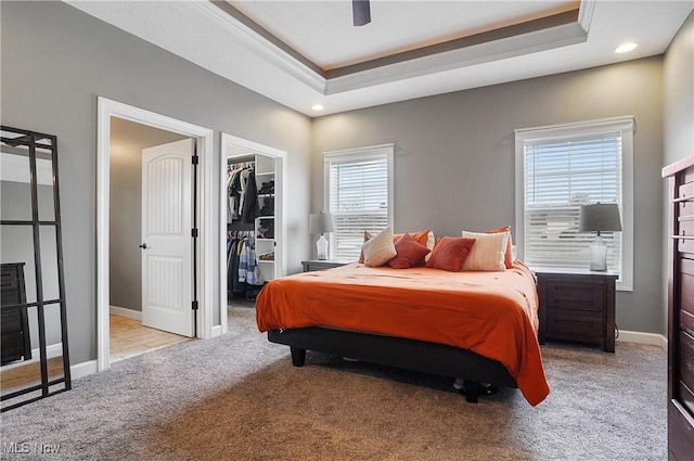 bedroom with light carpet, a spacious closet, a tray ceiling, and baseboards