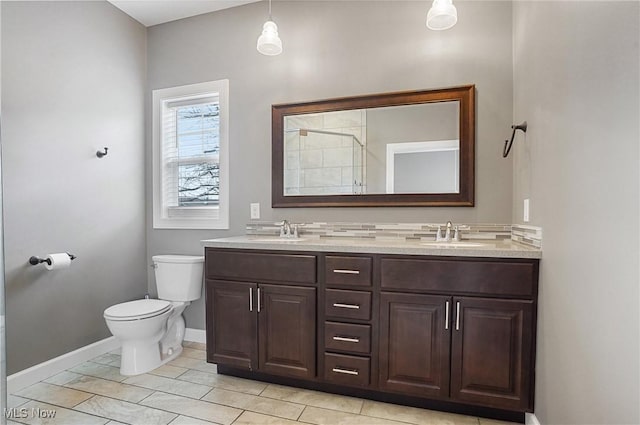 full bathroom featuring double vanity, tiled shower, a sink, and toilet