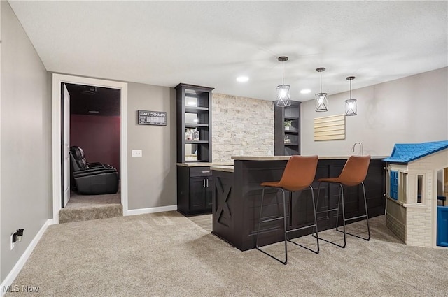 bar with baseboards, indoor wet bar, decorative light fixtures, and light colored carpet