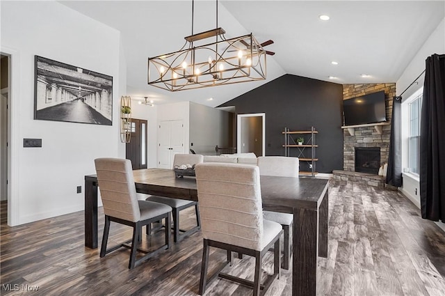 dining area featuring dark wood-style floors, lofted ceiling, a stone fireplace, a chandelier, and baseboards