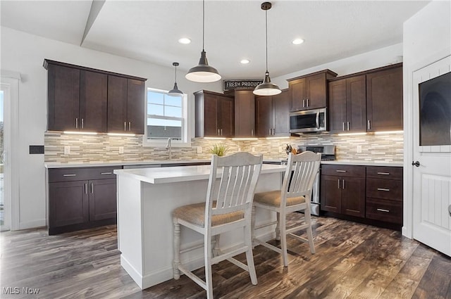 kitchen featuring a kitchen island, stainless steel microwave, light countertops, dark brown cabinets, and pendant lighting